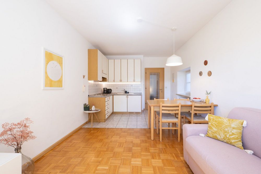 Heller Wohn- und Essbereich der Ferienwohnung Sonnenburg mit Küchenzeile, Esstisch, Holzparkett und rosafarbenem Sofa.
