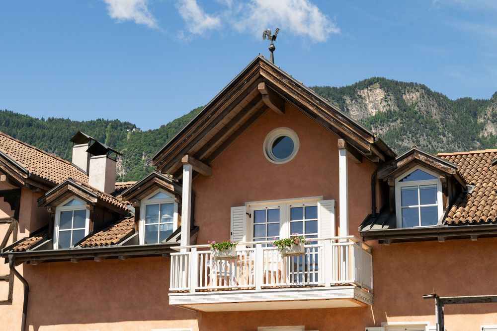 Detailansicht der Ferienwohnung Sonnenburg mit weißem Balkon, Blumenkästen und traditionellem Giebeldach vor Südtiroler Bergkulisse.