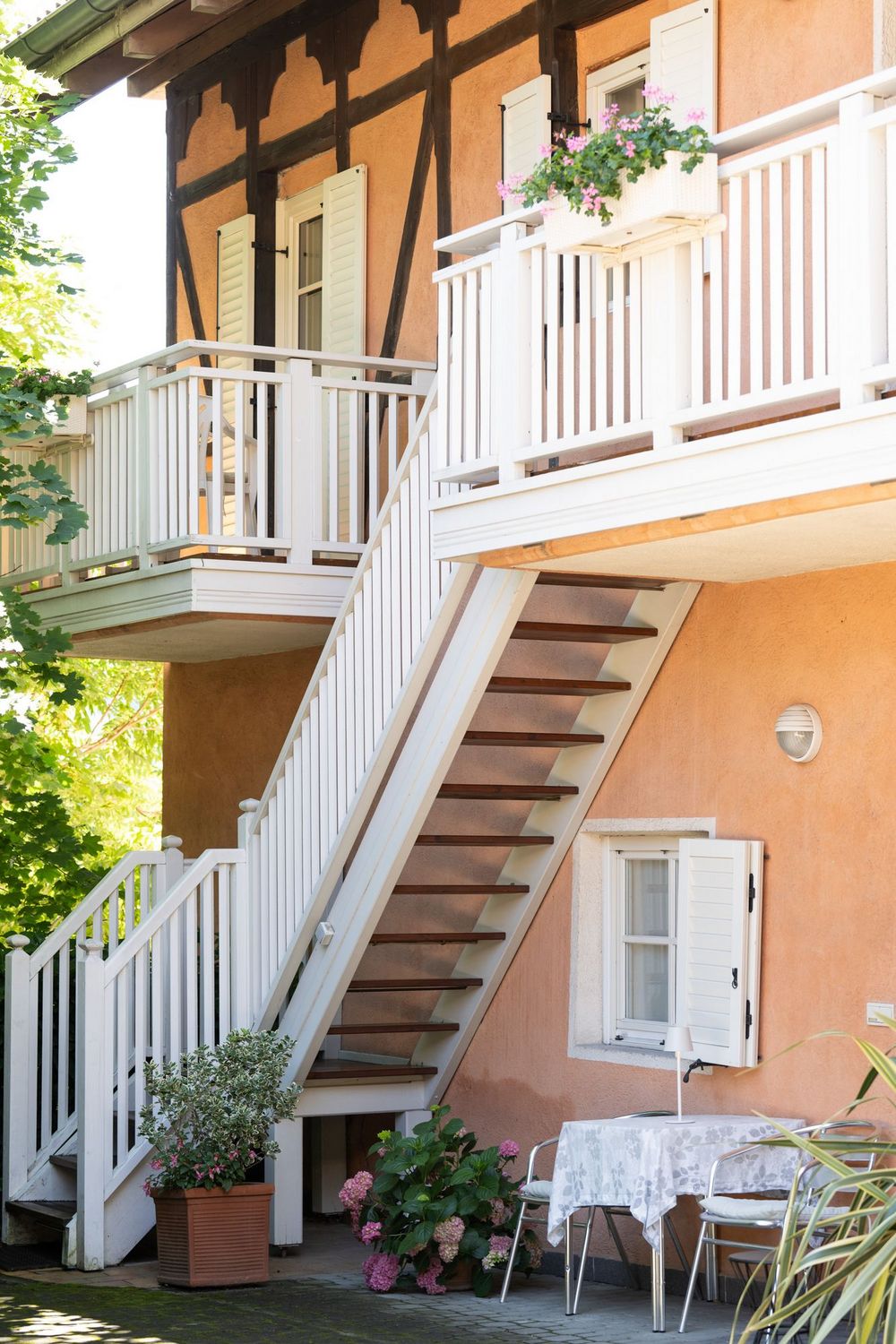 Weißer Treppenaufgang mit Balkonen und Blumenkästen im begrünten Innenhof der Ferienwohnung Sonnenburg.