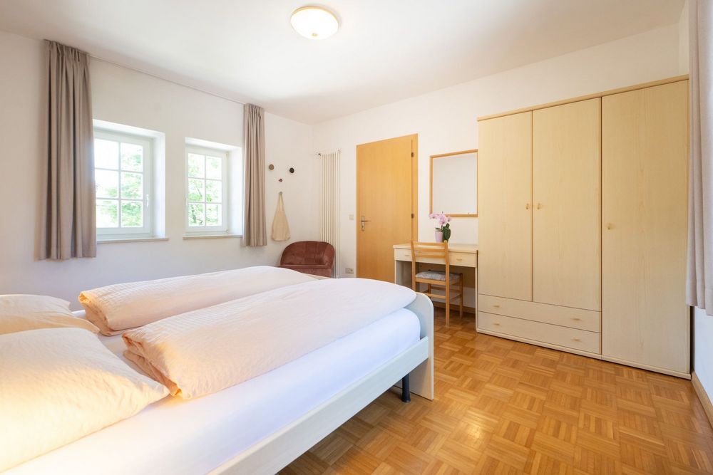 Helles Schlafzimmer der Ferienwohnung Sonnenburg mit Doppelbett, Holzparkett, großem Kleiderschrank und zwei Fenstern.