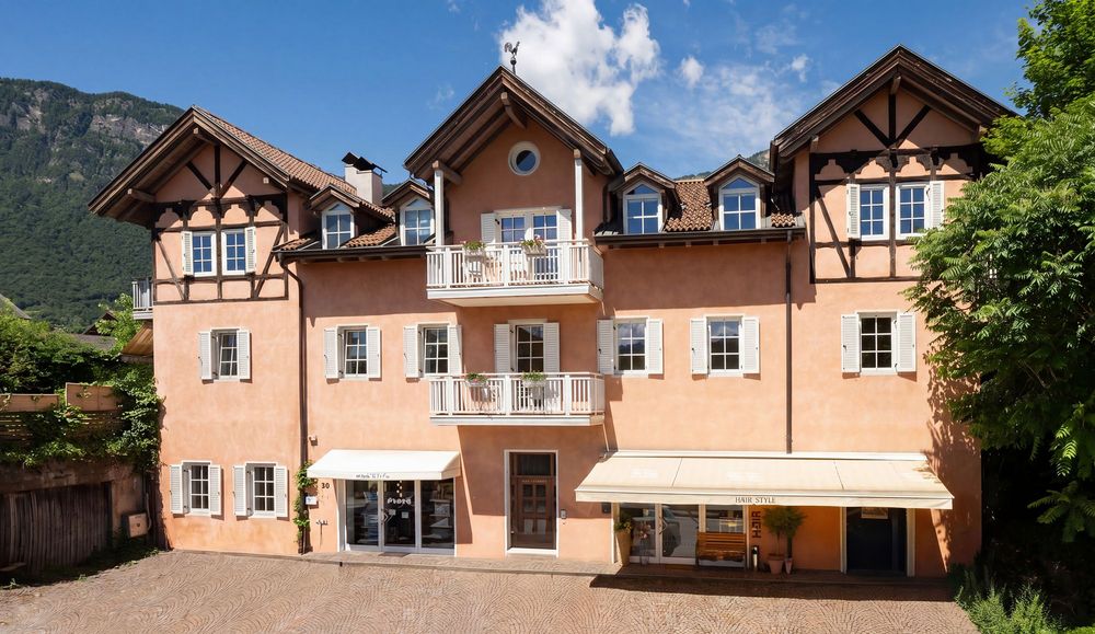 rosafarbenes Haus mit weißen Fensterläden und Balkonen vor einer grünen Bergkulisse in Südtirol.