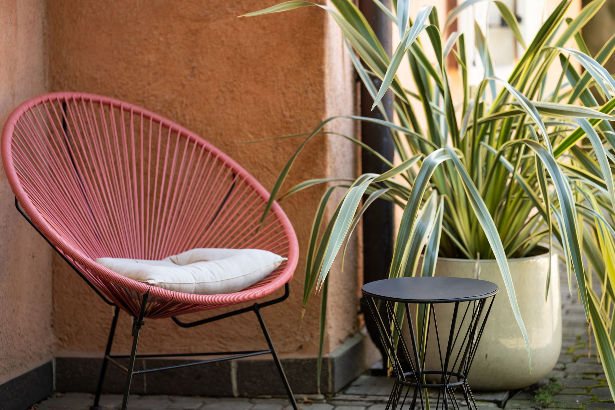 Rosa Loungesessel mit weißem Sitzkissen neben einem schwarzen Beistelltisch und großen Grünpflanzen auf der Terrasse der Ferienwohnung Sonnenburg.